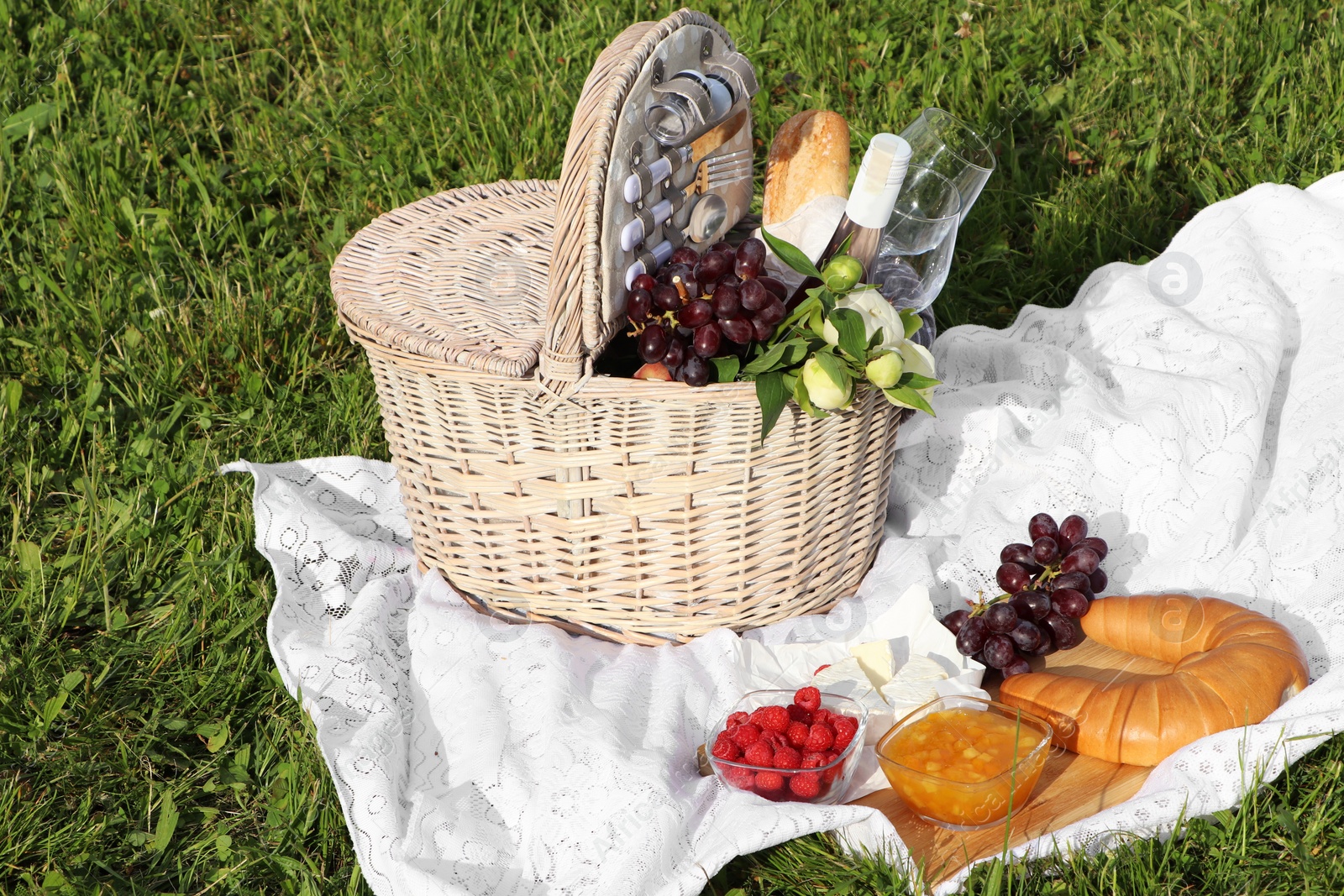 Photo of Picnic blanket with tasty food, flowers, basket and cider on green grass outdoors