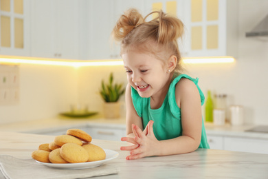 Photo of Cute little girl at table with cookies in kitchen