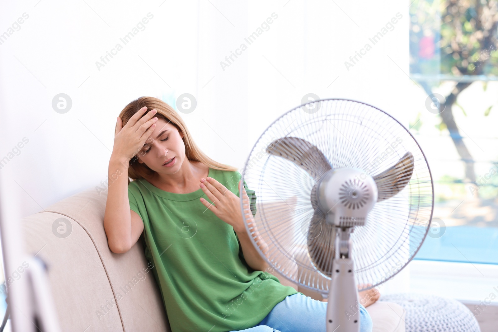 Photo of Woman suffering from heat in front of fan at home