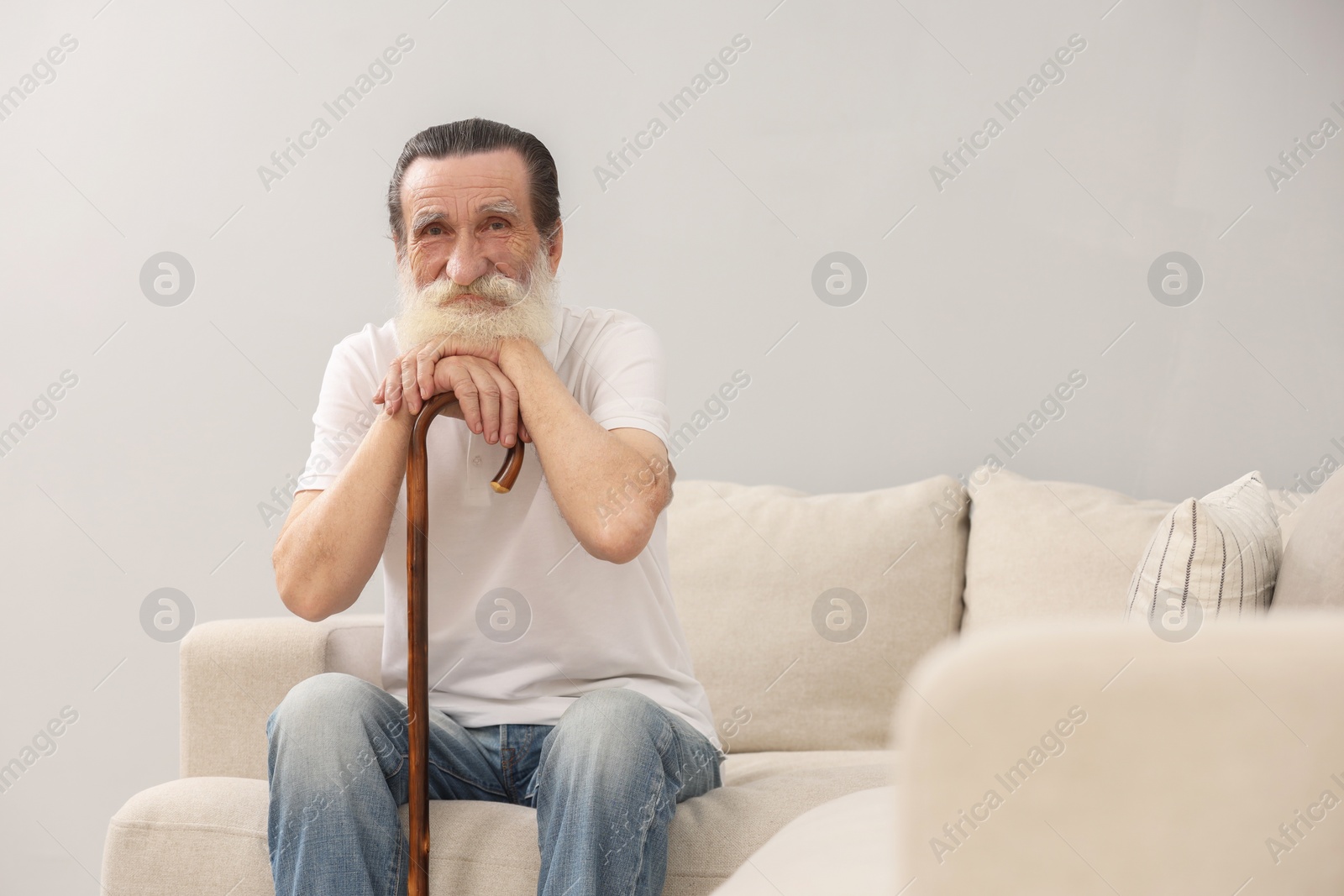 Photo of Senior man with walking cane on sofa indoors