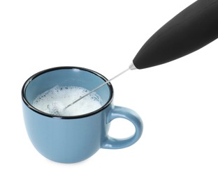 Photo of Whisking milk in cup with mini mixer (frother wand) isolated on white, closeup