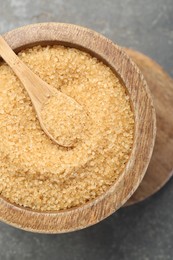 Brown sugar in bowl and spoon on grey table, top view