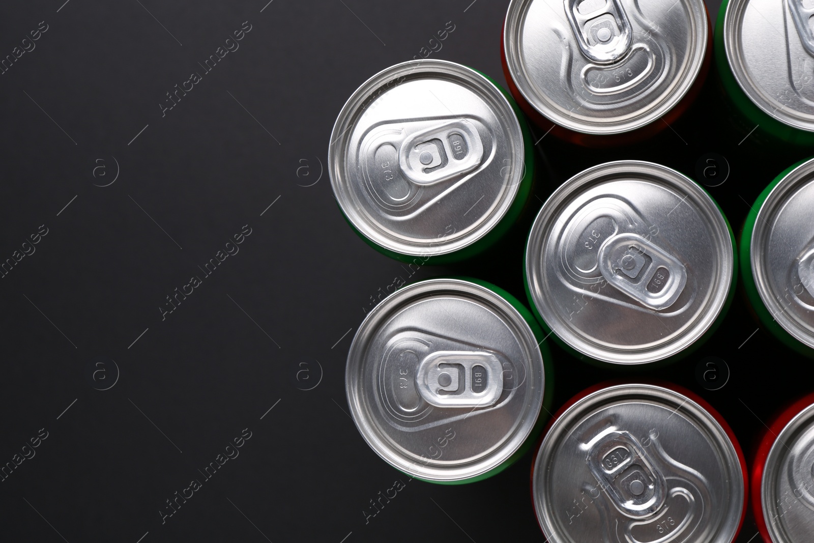 Photo of Energy drink in cans on black background, top view. Space for text