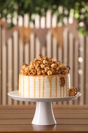 Photo of Caramel drip cake decorated with popcorn and pretzels on wooden table, space for text
