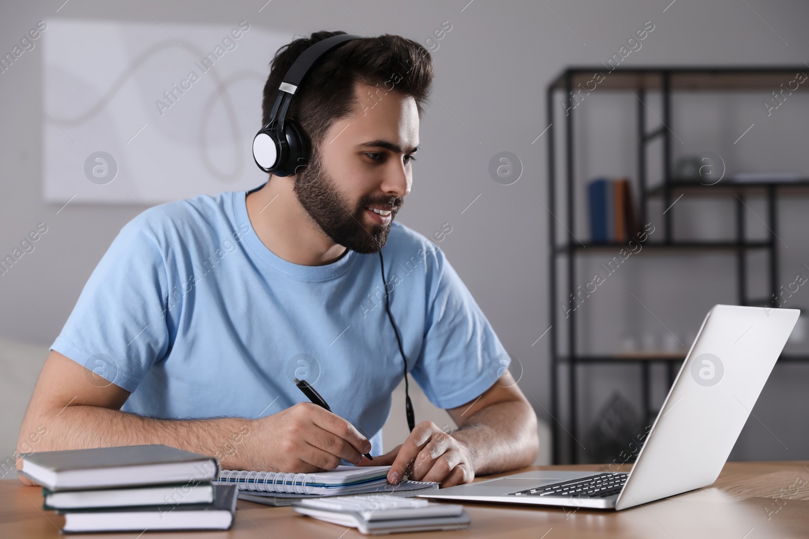 Photo of Young man watching webinar at table in room