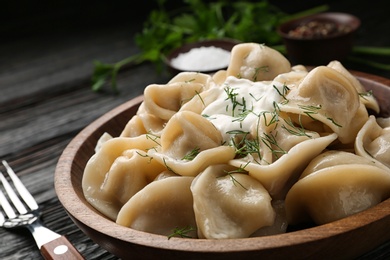 Photo of Tasty dumplings with sour cream in bowl on black wooden table, closeup