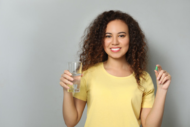 Photo of African-American woman with glass of water and vitamin capsule on light grey background