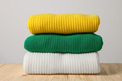 Photo of Stack of casual sweaters on wooden table against light background