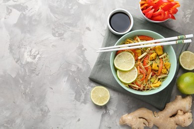 Photo of Stir-fry. Delicious cooked noodles with chicken and vegetables in bowl served on gray textured table, flat lay. Space for text