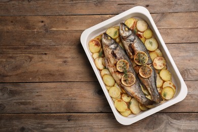 Photo of Baking tray with delicious baked sea bass fish and potatoes on wooden table, top view. Space for text