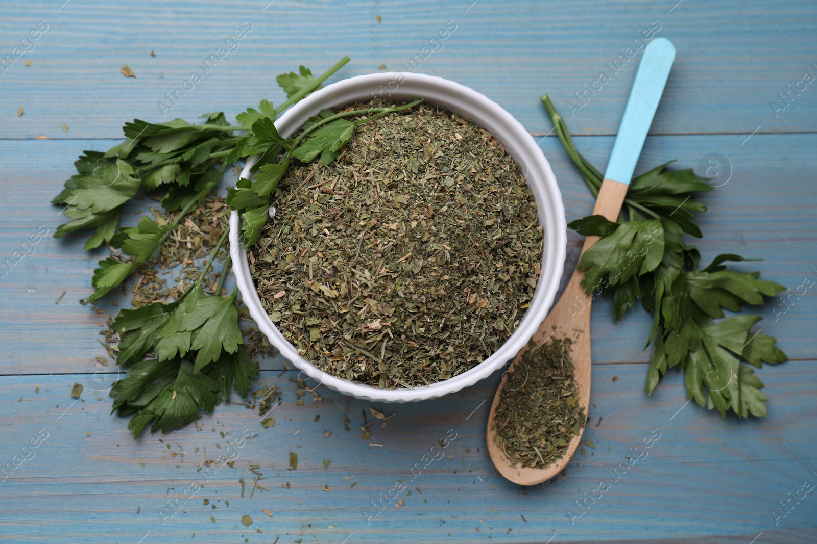 Photo of Dried parsley and fresh leaves on light blue wooden table, flat lay