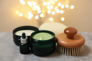 Photo of Natural scrub and other body care products on grey table against blurred lights