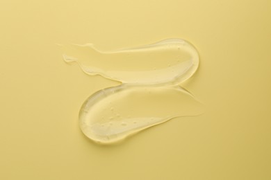 Photo of Sample of clear cosmetic gel on yellow background, top view