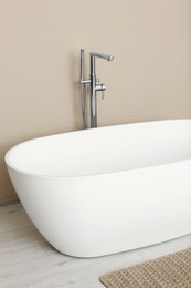 Photo of Beautiful white tub near beige wall in bathroom. Interior design