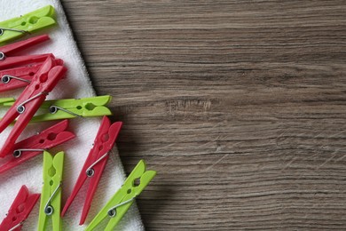 Photo of Colorful plastic clothespins and towel on wooden background, top view Space for text