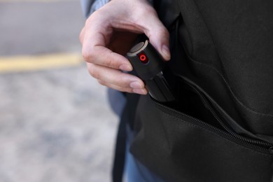 Photo of Man putting pepper spray into backpack outdoors, closeup. Space for text