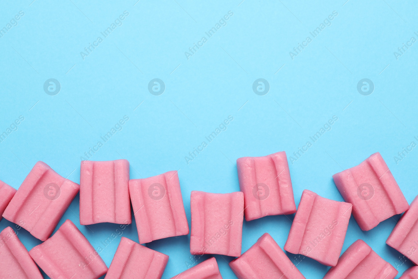 Photo of Tasty pink chewing gums on light blue background, flat lay. Space for text