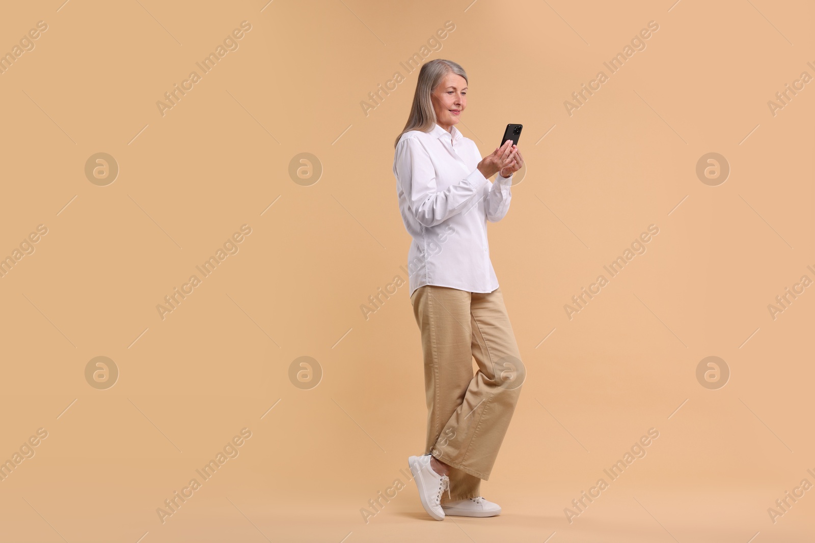 Photo of Senior woman with phone on beige background, space for text