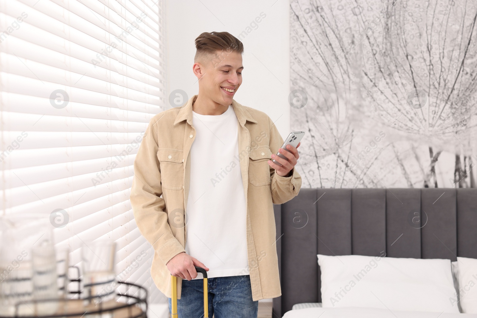 Photo of Smiling guest with smartphone in stylish hotel room