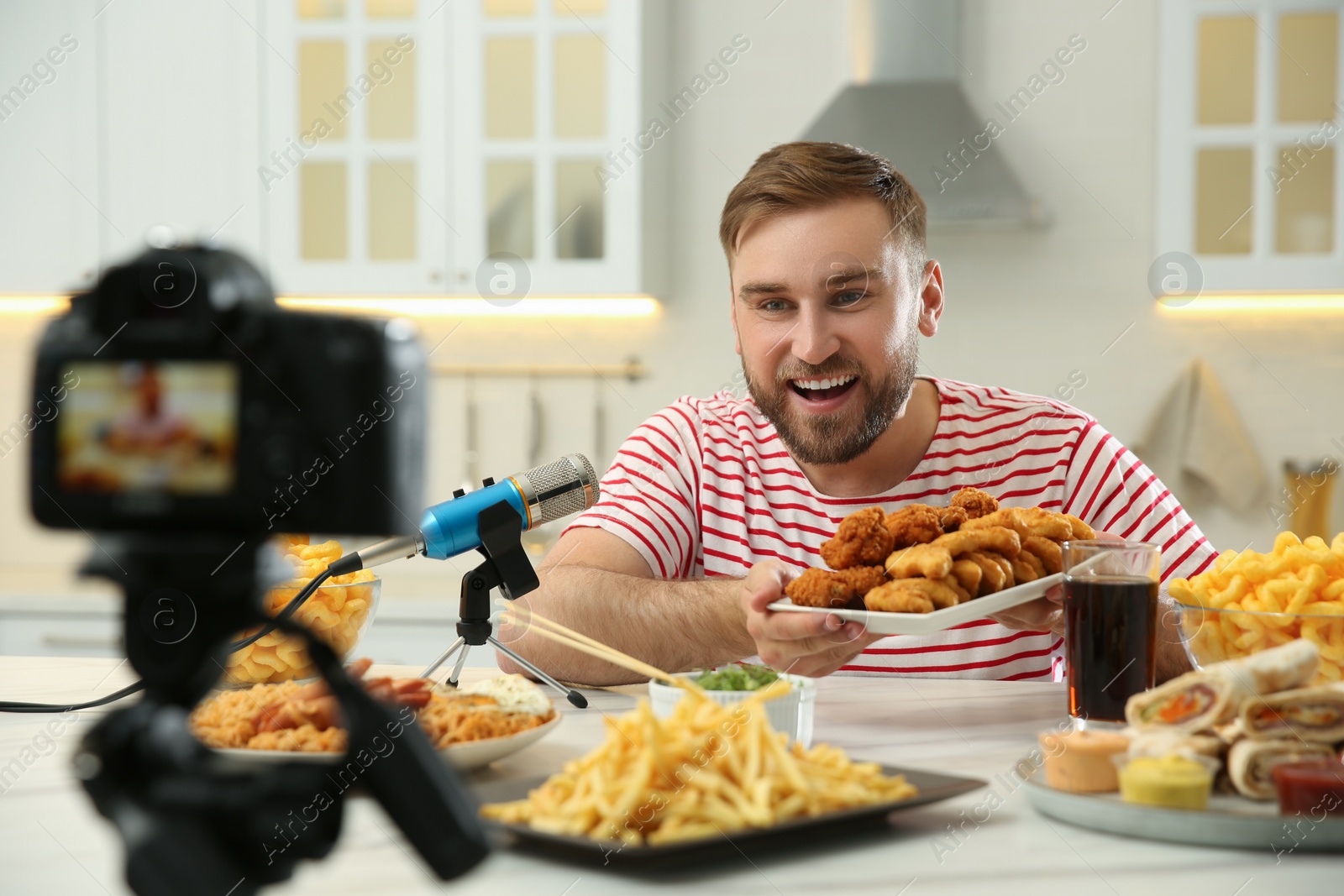 Photo of Food blogger recording eating show on camera in kitchen. Mukbang vlog