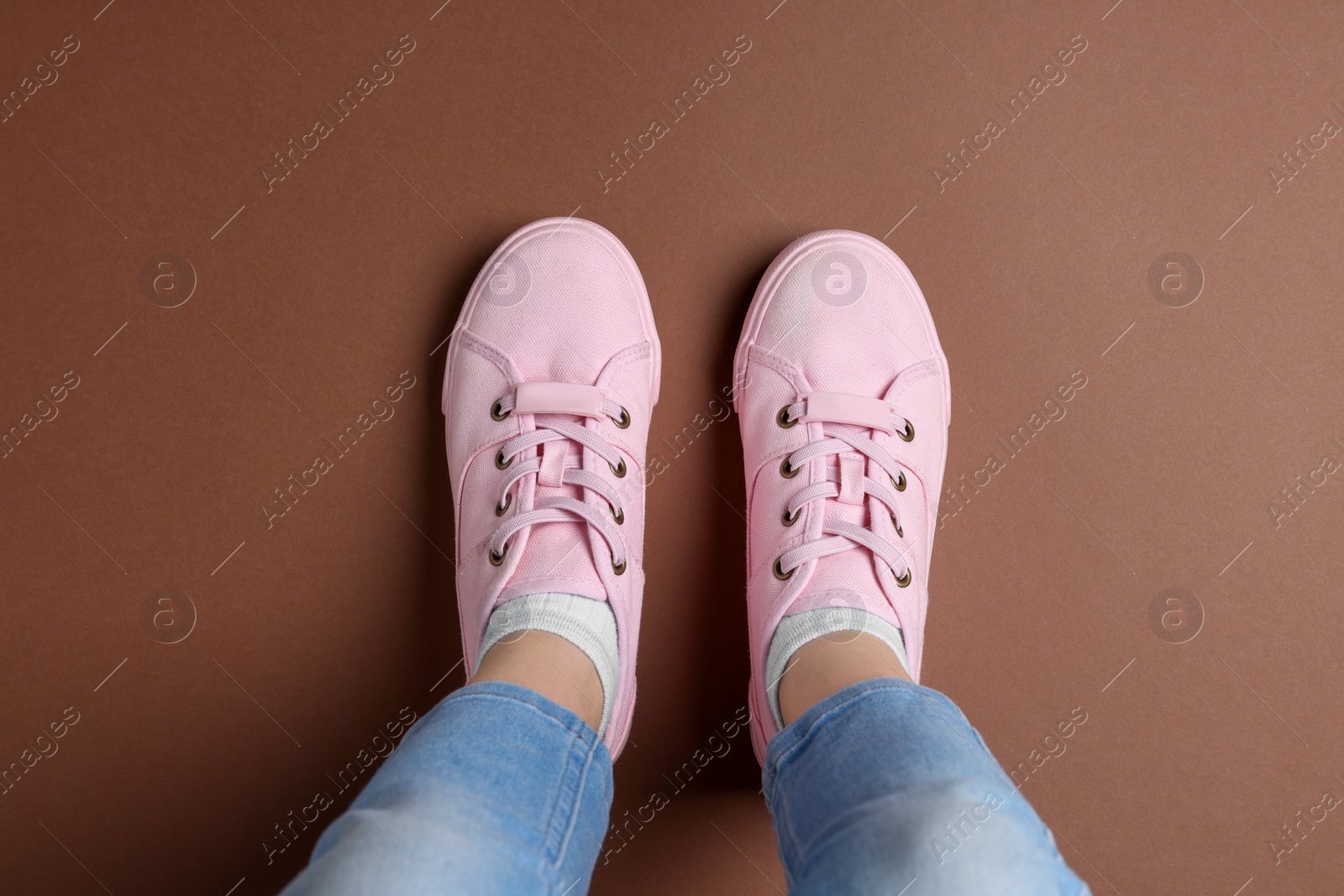 Photo of Woman in stylish sneakers standing on brown background, top view