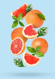 Image of Tasty ripe grapefruits and green leaves falling on light blue background