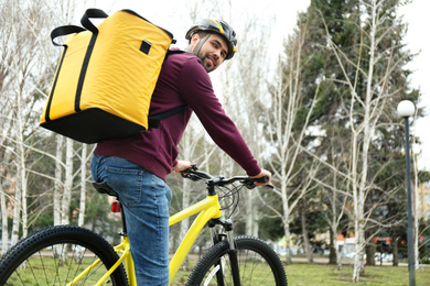 Courier with thermo bag riding bicycle outdoors. Food delivery service