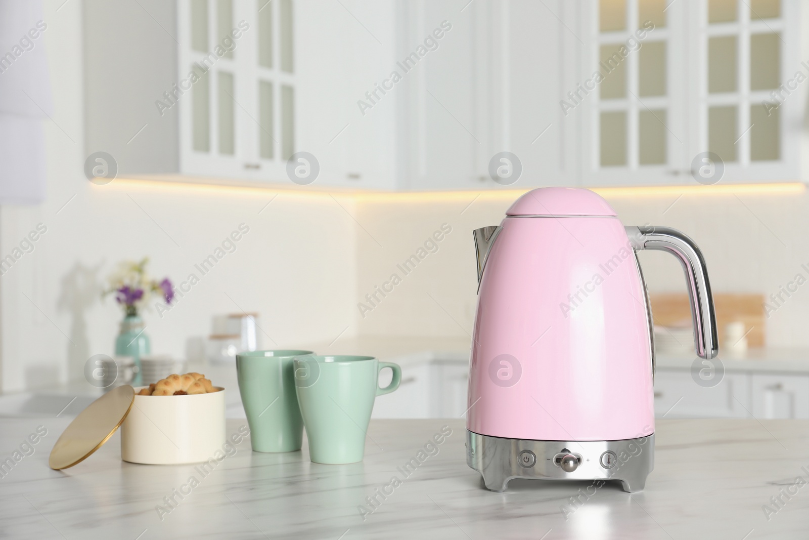 Photo of Modern electric kettle, cups and cookies on table in kitchen