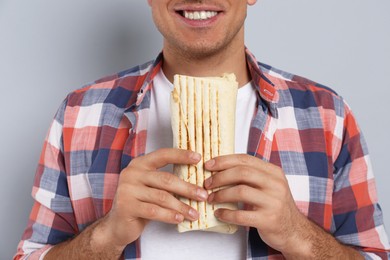 Man with delicious shawarma on grey background, closeup