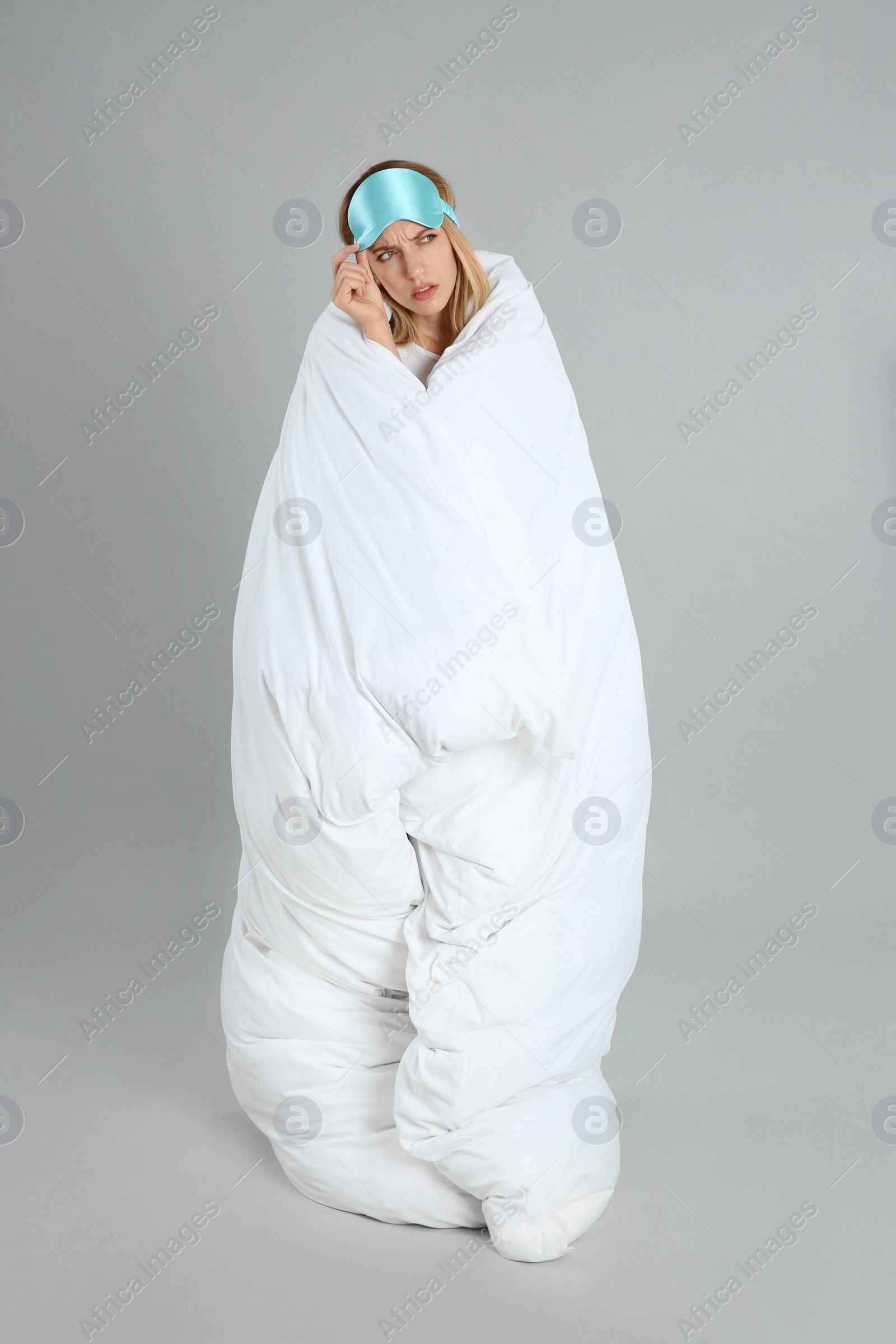 Photo of Emotional young woman in sleeping mask wrapped with soft blanket on grey background