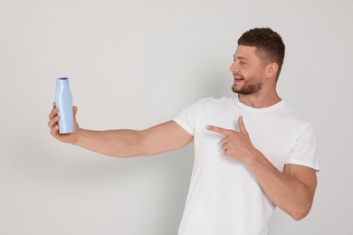 Photo of Handsome young man holding bottle of shampoo on white background