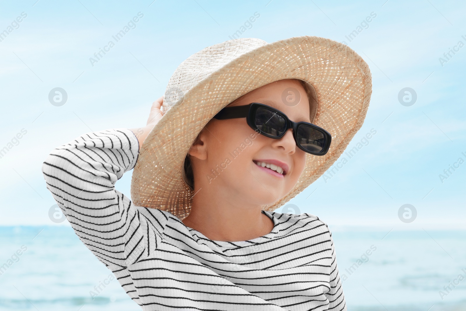 Photo of Little girl wearing sunglasses and hat at beach on sunny day