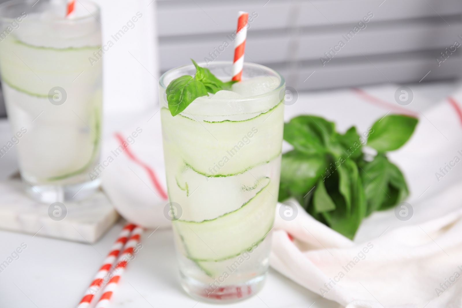 Photo of Glasses of refreshing cucumber water with basil on white table