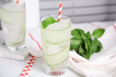 Photo of Glasses of refreshing cucumber water with basil on white table