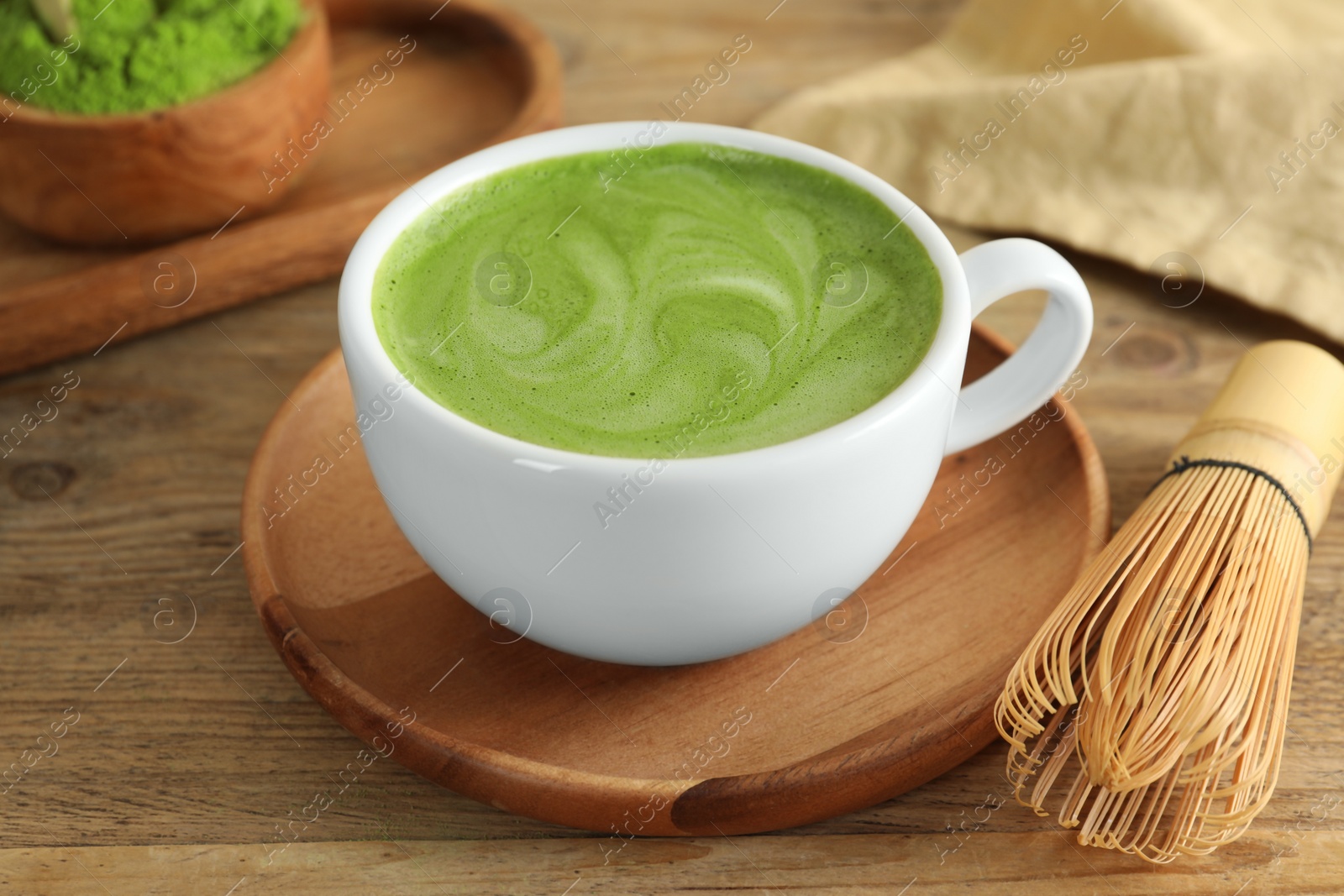 Photo of Cup of fresh matcha latte and bamboo whisk on wooden table, closeup