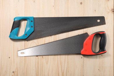 Photo of Saws with colorful handles on wooden background, flat lay