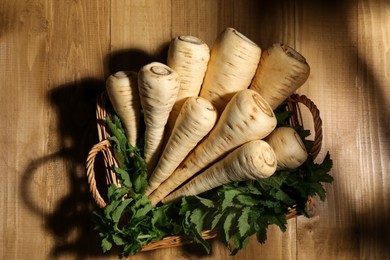 Wicker basket with delicious fresh ripe parsnips and green leaves on wooden table, top view