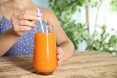 Photo of Woman with glass of freshly made carrot juice at wooden table, closeup