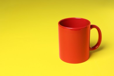 Photo of One red ceramic mug on yellow background, space for text
