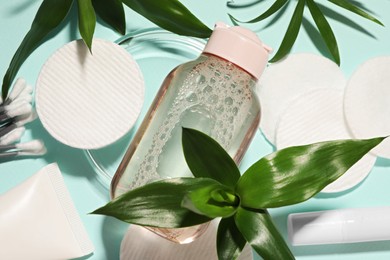 Photo of Bottle of micellar cleansing water, cotton pads and green plants on turquoise background, flat lay