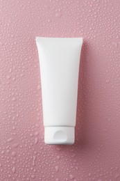 Moisturizing cream in tube on pink background with water drops, top view