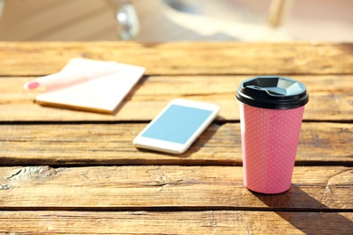 Photo of Cardboard cup of coffee and mobile phone on wooden table