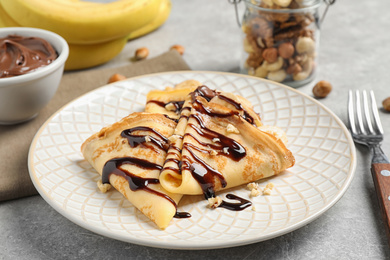 Photo of Delicious thin pancakes with chocolate spread, banana and nuts on light table