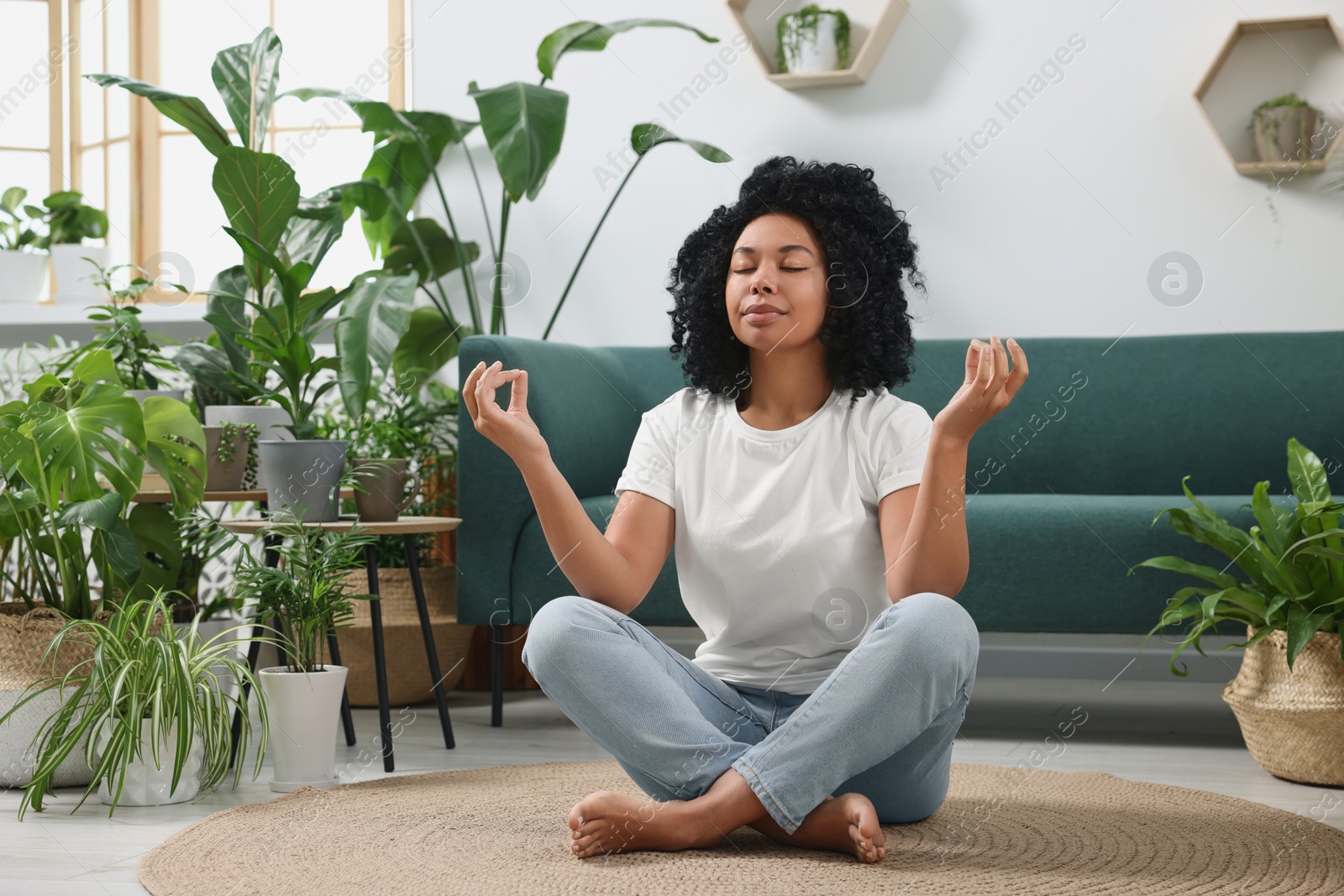 Photo of Relaxing atmosphere. Woman meditating near potted houseplants in room