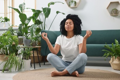 Relaxing atmosphere. Woman meditating near potted houseplants in room