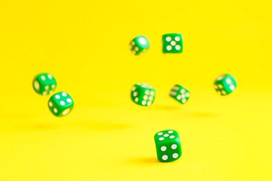 Photo of Many green game dices falling on yellow background