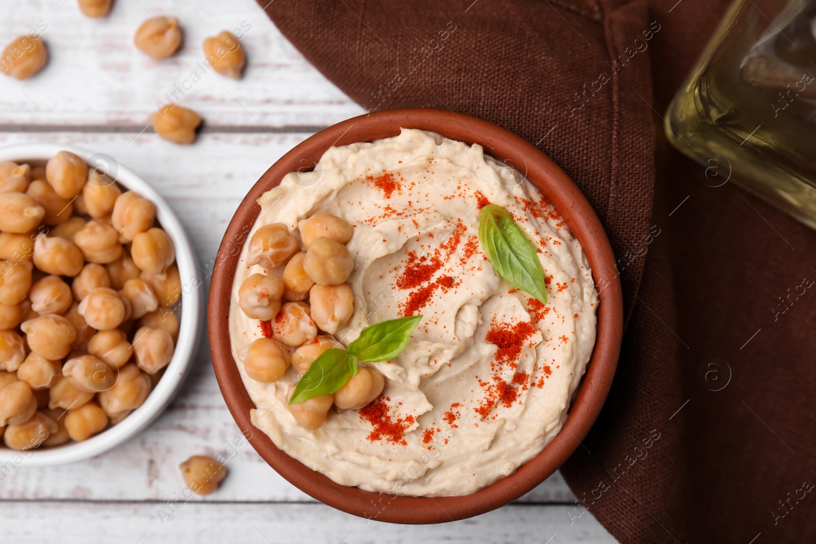 Photo of Delicious hummus with chickpeas and paprika served on white wooden table, flat lay