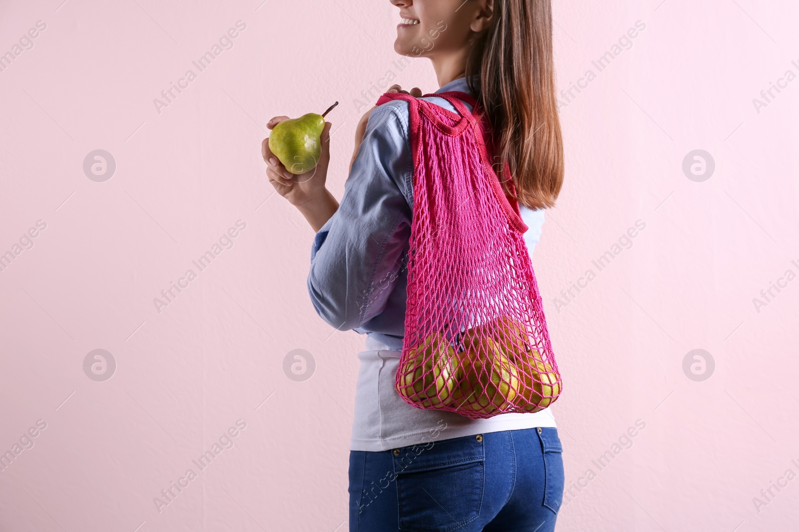 Photo of Woman holding net bag with fresh ripe pears on pink background, closeup