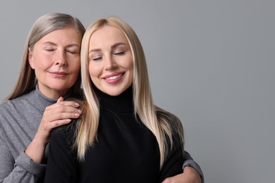 Family portrait of young woman and her mother on grey background. Space for text