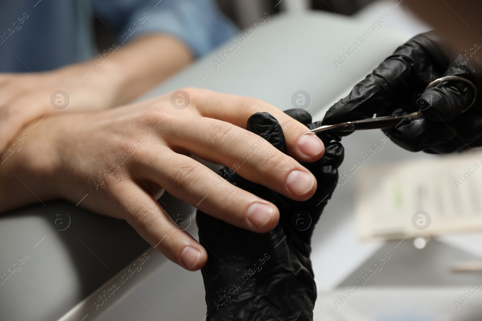 Photo of Professional manicurist cutting client's cuticle in beauty salon, closeup